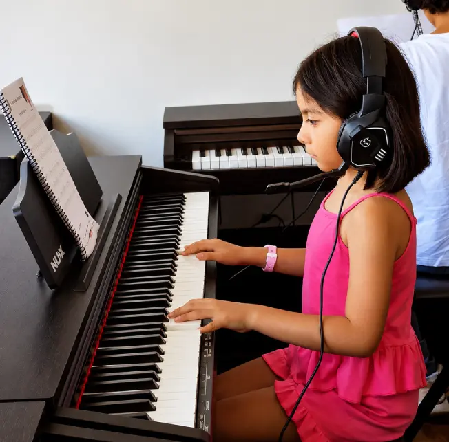 Niña en clases de piano con audífonos en la academia de música